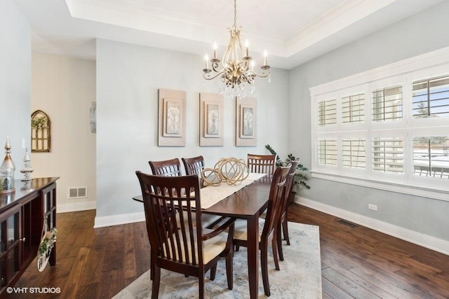 dining room featuring dark wood-type flooring, a raised ceiling, and visible vents