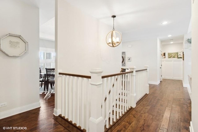 hallway featuring dark wood-type flooring, baseboards, an upstairs landing, and an inviting chandelier