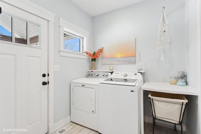 clothes washing area with laundry area, visible vents, baseboards, washer and dryer, and light wood-style floors