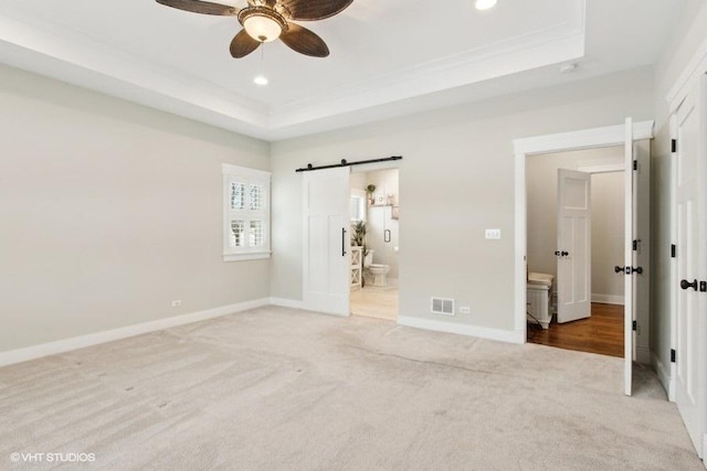 unfurnished bedroom with visible vents, a tray ceiling, baseboards, and a barn door