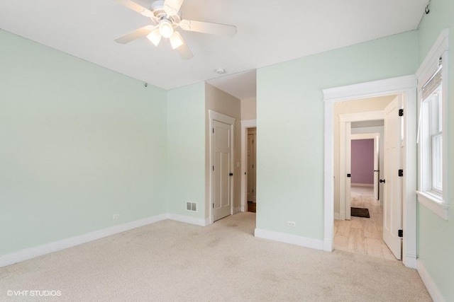 unfurnished bedroom featuring a ceiling fan, light colored carpet, visible vents, and baseboards