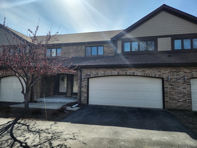 townhome / multi-family property with aphalt driveway, brick siding, and a shingled roof