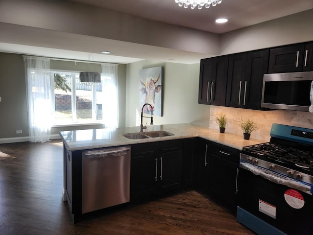 kitchen featuring stainless steel appliances, a peninsula, a sink, dark cabinetry, and light stone countertops