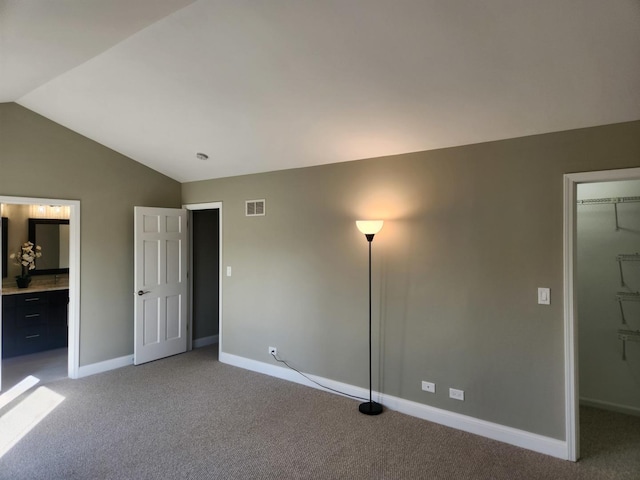 unfurnished bedroom featuring light carpet, a spacious closet, visible vents, and vaulted ceiling