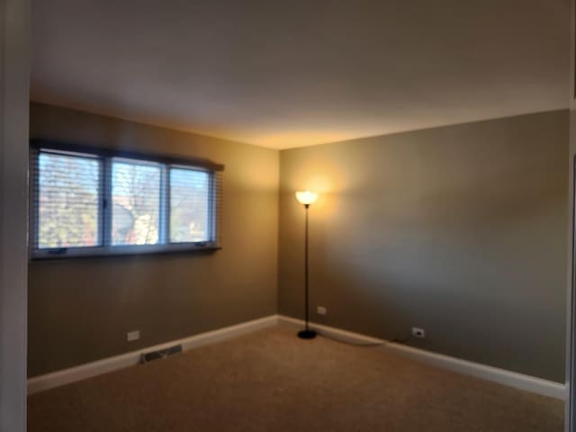 spare room with carpet flooring, visible vents, and baseboards