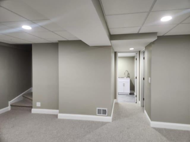 finished basement featuring a paneled ceiling, carpet, visible vents, and baseboards