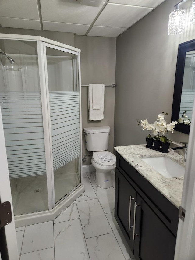 bathroom featuring a drop ceiling, toilet, vanity, marble finish floor, and a shower stall