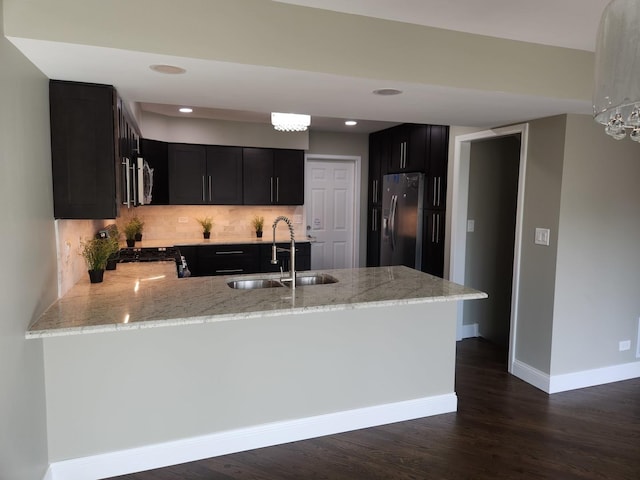 kitchen with dark cabinets, a sink, refrigerator with ice dispenser, light stone countertops, and stainless steel microwave