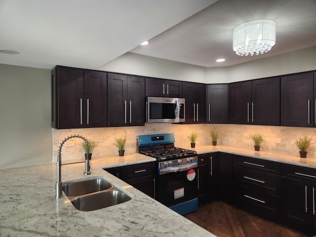 kitchen featuring appliances with stainless steel finishes, a sink, light stone counters, and tasteful backsplash