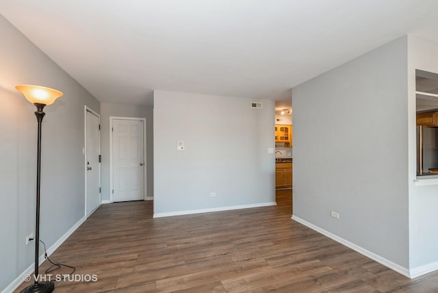 unfurnished living room featuring visible vents, a sink, baseboards, and wood finished floors