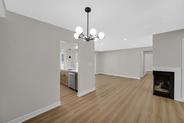 unfurnished living room with light wood finished floors, baseboards, an inviting chandelier, a fireplace, and a sink