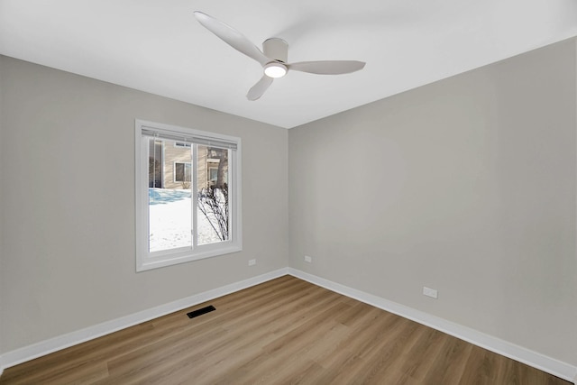 empty room with a ceiling fan, wood finished floors, visible vents, and baseboards