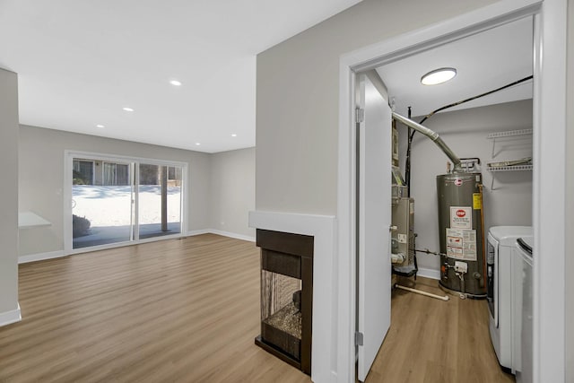 living area featuring light wood-type flooring, baseboards, gas water heater, and washing machine and clothes dryer