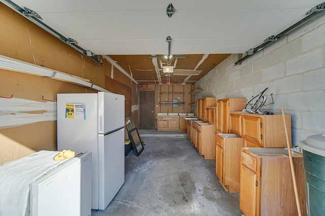 garage with concrete block wall, freestanding refrigerator, and a garage door opener