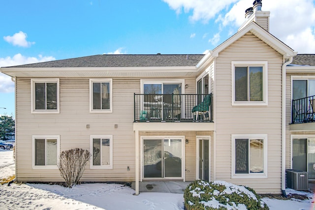 snow covered back of property featuring a chimney and central AC unit