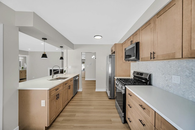 kitchen with light countertops, hanging light fixtures, light wood-style flooring, appliances with stainless steel finishes, and a sink