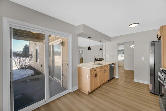 kitchen featuring light wood-style flooring, stainless steel appliances, a sink, light countertops, and pendant lighting