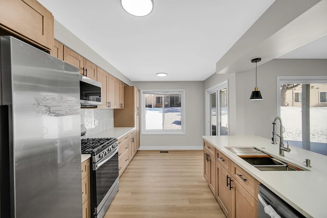 kitchen featuring stainless steel appliances, pendant lighting, light countertops, and a sink