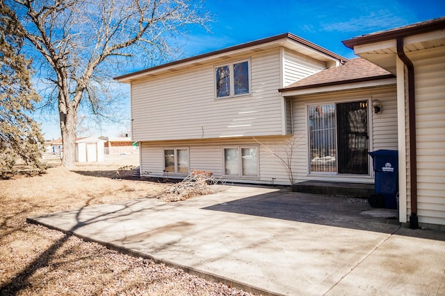 back of house featuring a shingled roof, a patio, an outdoor structure, and a storage unit