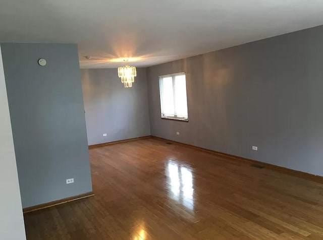 spare room with a chandelier, baseboards, and wood finished floors