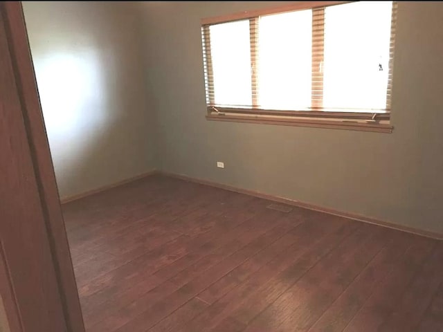 spare room featuring baseboards and dark wood-type flooring