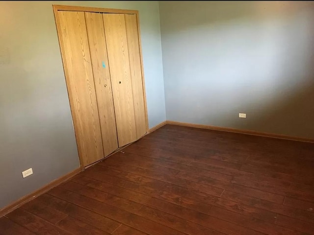 unfurnished bedroom featuring dark wood-type flooring, a closet, and baseboards