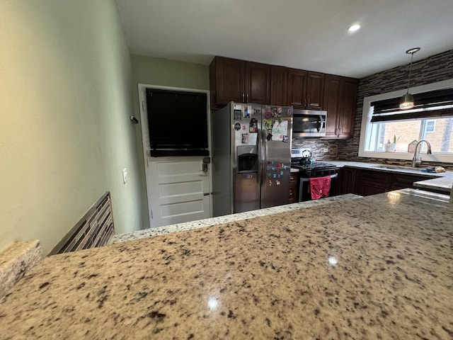 kitchen featuring decorative light fixtures, backsplash, appliances with stainless steel finishes, a sink, and light stone countertops