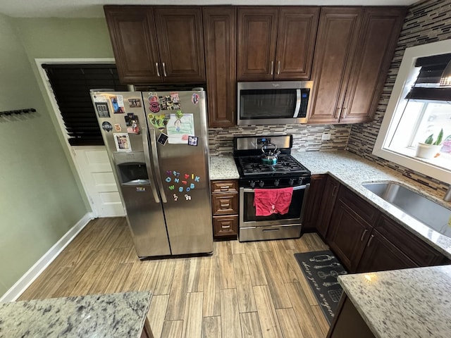 kitchen featuring decorative backsplash, appliances with stainless steel finishes, light stone countertops, light wood-type flooring, and a sink