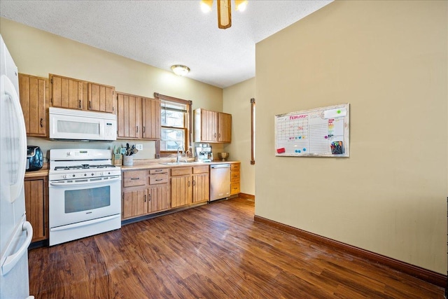 kitchen with white appliances, dark wood-type flooring, light countertops, a textured ceiling, and a sink