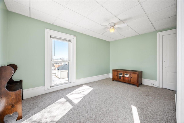 empty room featuring light carpet, ceiling fan, a drop ceiling, and baseboards