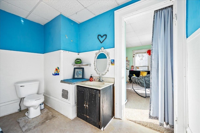 bathroom featuring toilet, concrete flooring, a drop ceiling, and vanity