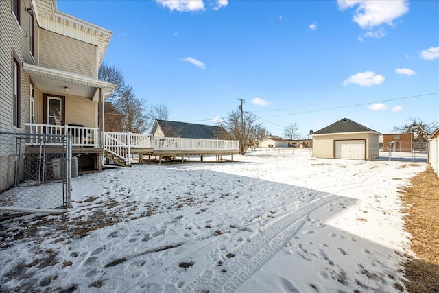 snowy yard featuring a wooden deck, a detached garage, and an outdoor structure