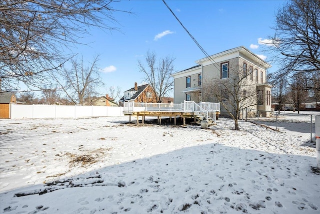 snow covered rear of property with fence and a wooden deck