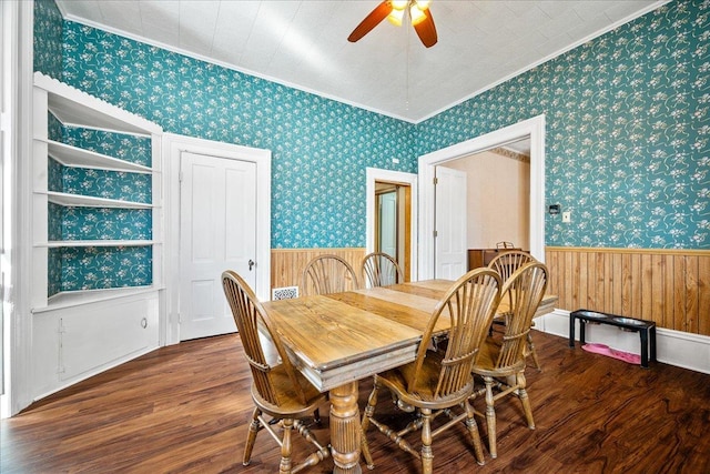 dining space featuring wallpapered walls, a ceiling fan, a wainscoted wall, wood finished floors, and crown molding