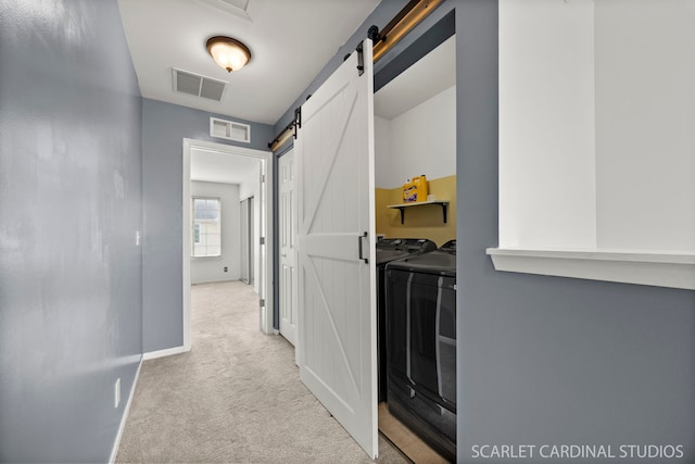 hallway with light carpet, a barn door, visible vents, and washer and dryer