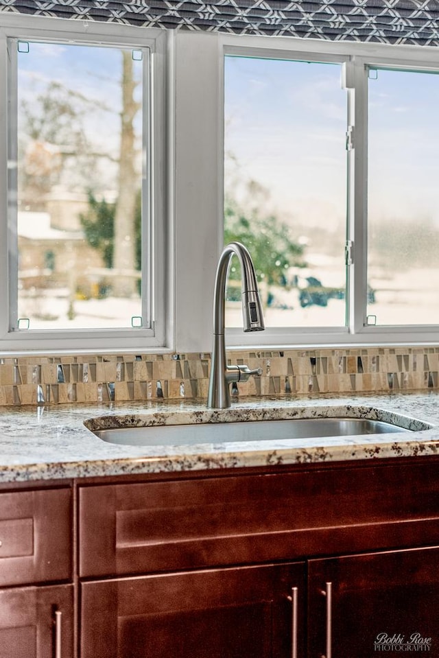 room details with reddish brown cabinets, tasteful backsplash, glass insert cabinets, light stone countertops, and a sink