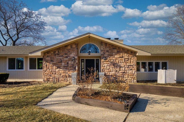 entrance to property featuring stone siding and a shingled roof