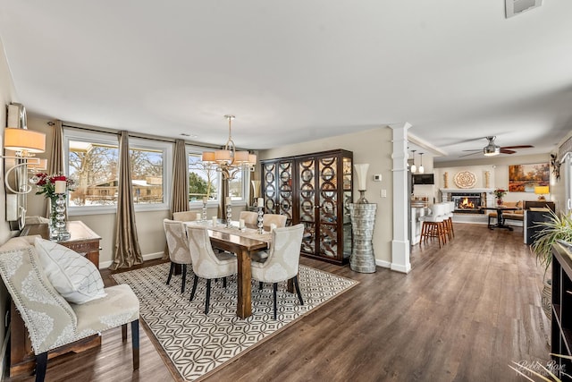 dining space featuring decorative columns, visible vents, dark wood finished floors, and a glass covered fireplace