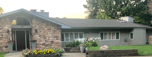 exterior space with stone siding, a shingled roof, and a chimney