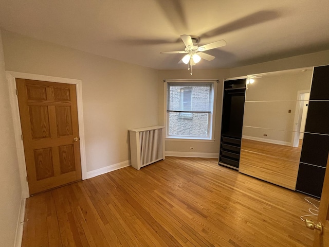 unfurnished bedroom with ceiling fan, radiator, light wood-type flooring, and baseboards