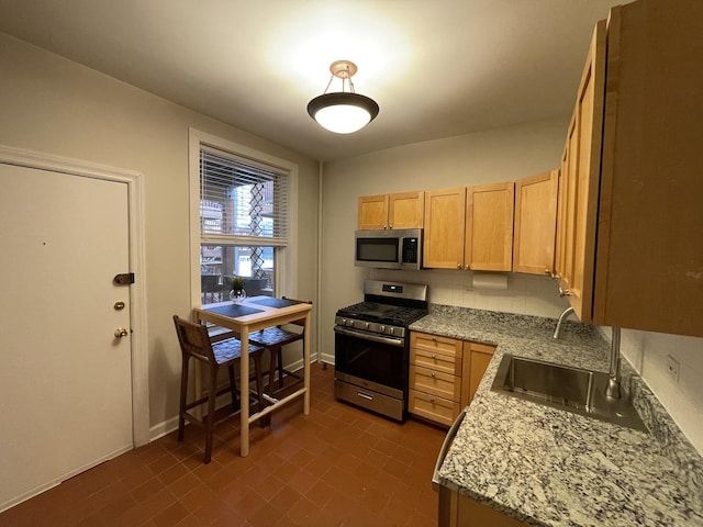 kitchen featuring light brown cabinets, a sink, appliances with stainless steel finishes, baseboards, and light stone countertops