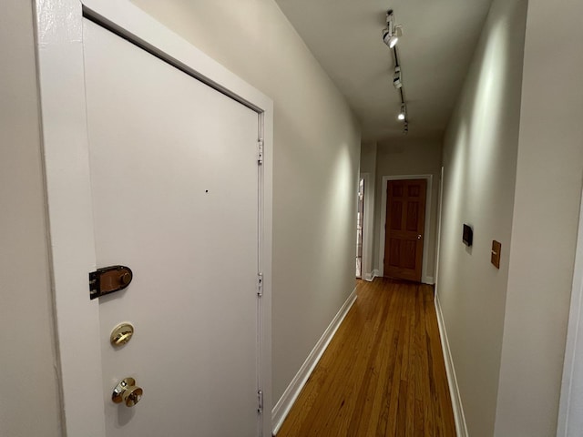 hallway featuring baseboards, dark wood-type flooring, and track lighting