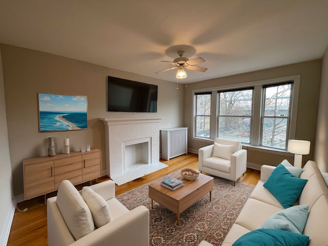 living room with a fireplace, light wood-style floors, baseboards, and ceiling fan