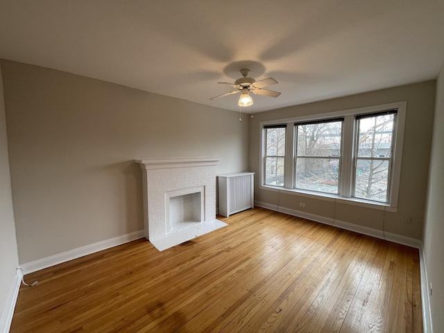 unfurnished living room featuring a ceiling fan, radiator heating unit, wood-type flooring, a fireplace, and baseboards