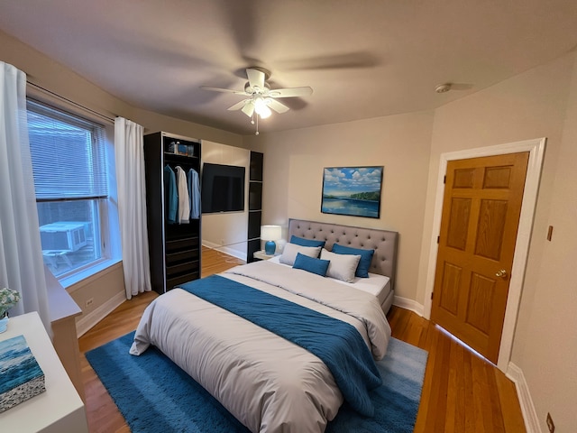 bedroom featuring cooling unit, baseboards, light wood-style flooring, and a ceiling fan