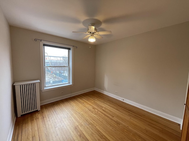 spare room featuring light wood-type flooring, baseboards, a ceiling fan, and radiator heating unit