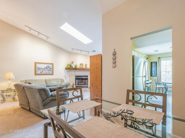 dining area featuring a tiled fireplace, a skylight, rail lighting, and light carpet