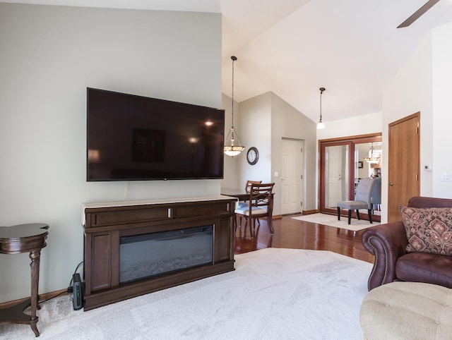 living area with baseboards, vaulted ceiling, wood finished floors, and a glass covered fireplace