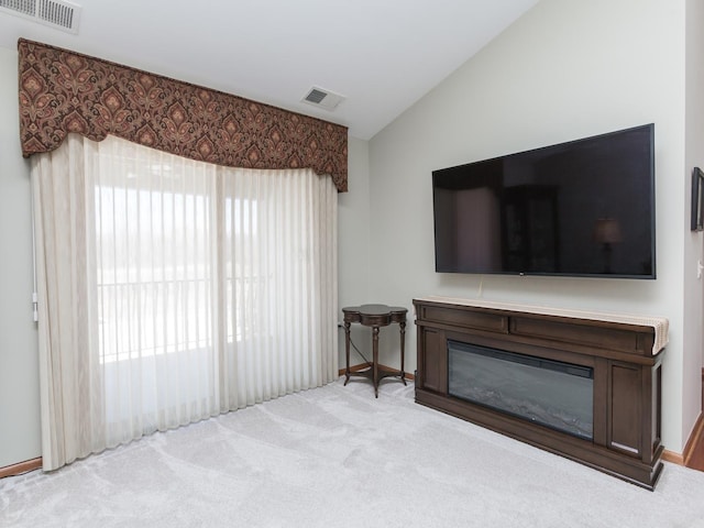 living room featuring lofted ceiling, a glass covered fireplace, visible vents, and light colored carpet