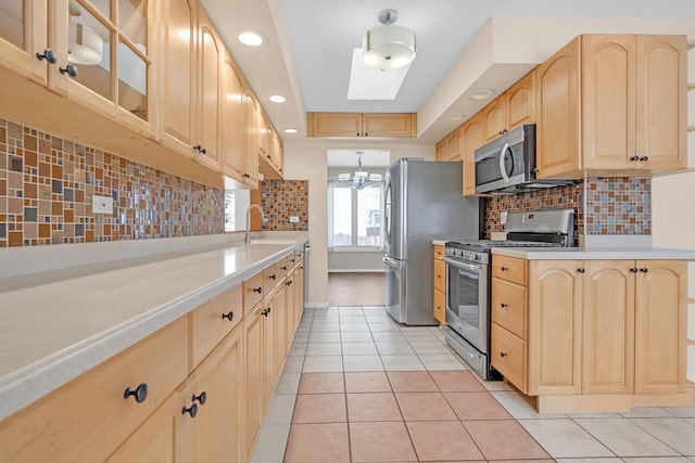 kitchen featuring pendant lighting, light countertops, appliances with stainless steel finishes, light brown cabinets, and a sink